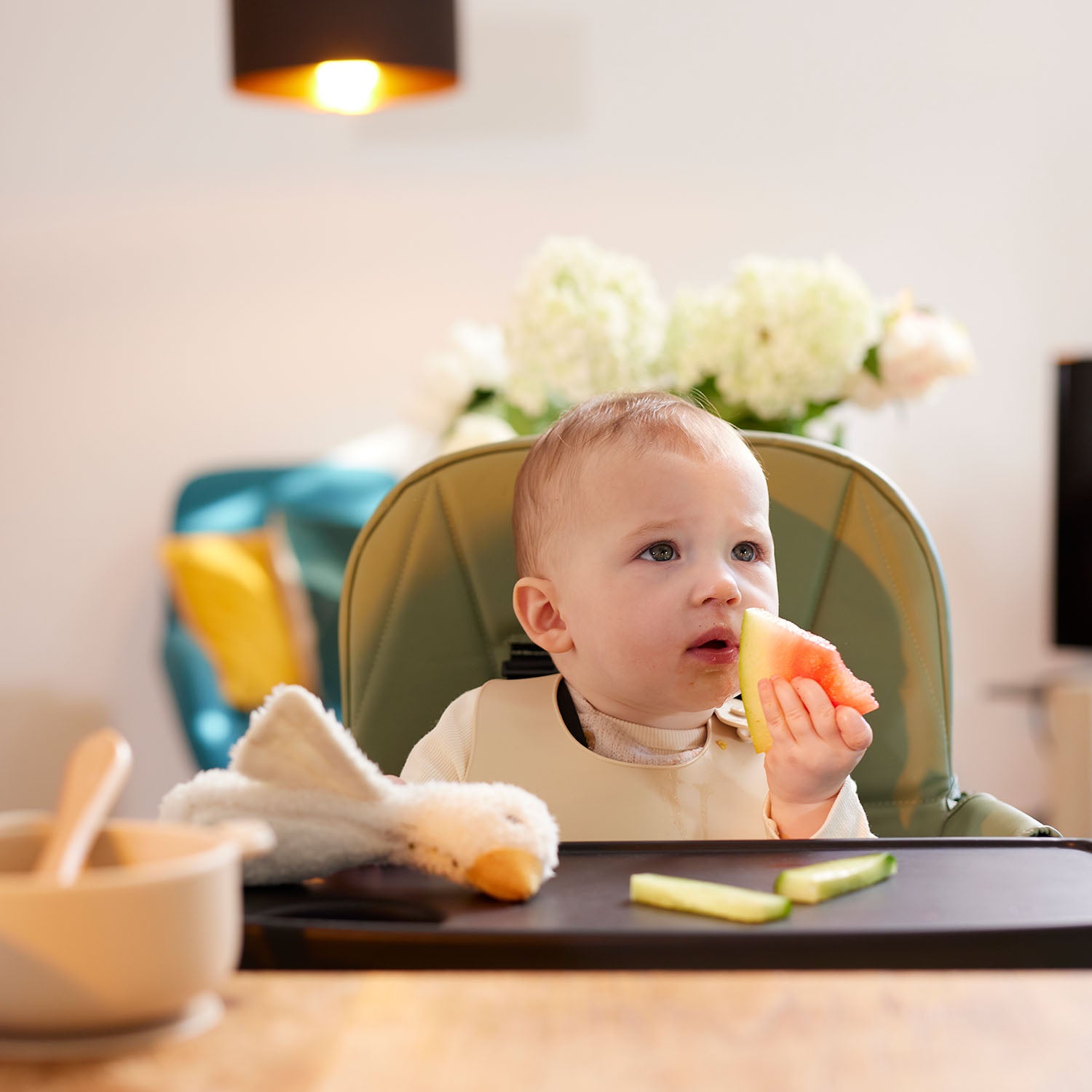 Baby hold a slide of watermelon while sitting on Ickle Bubba Flip Magic Fold Highchair
