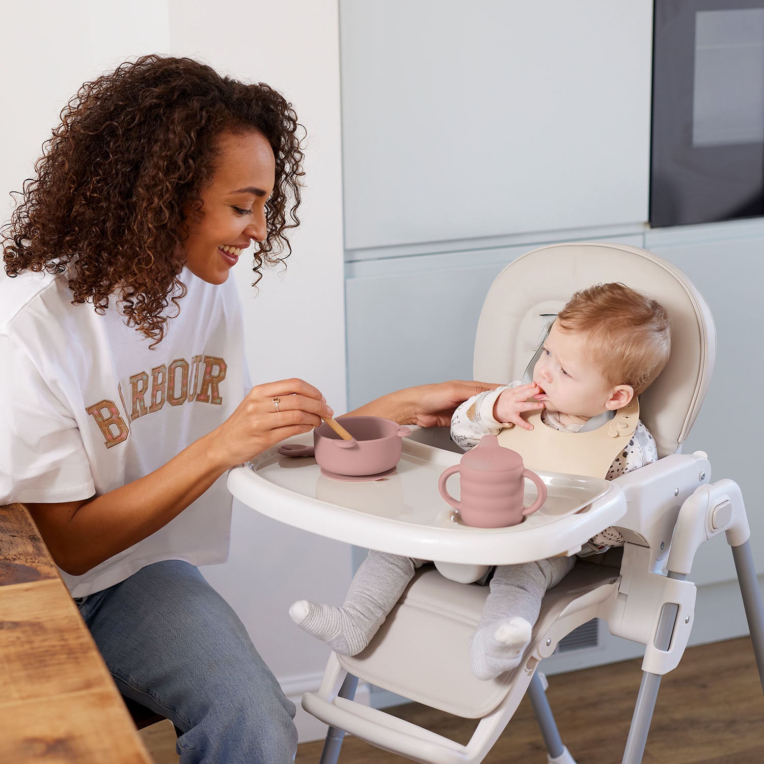 Woman giving food to a child sitting in Ickle Bubba Switch Multi Function Highchair
